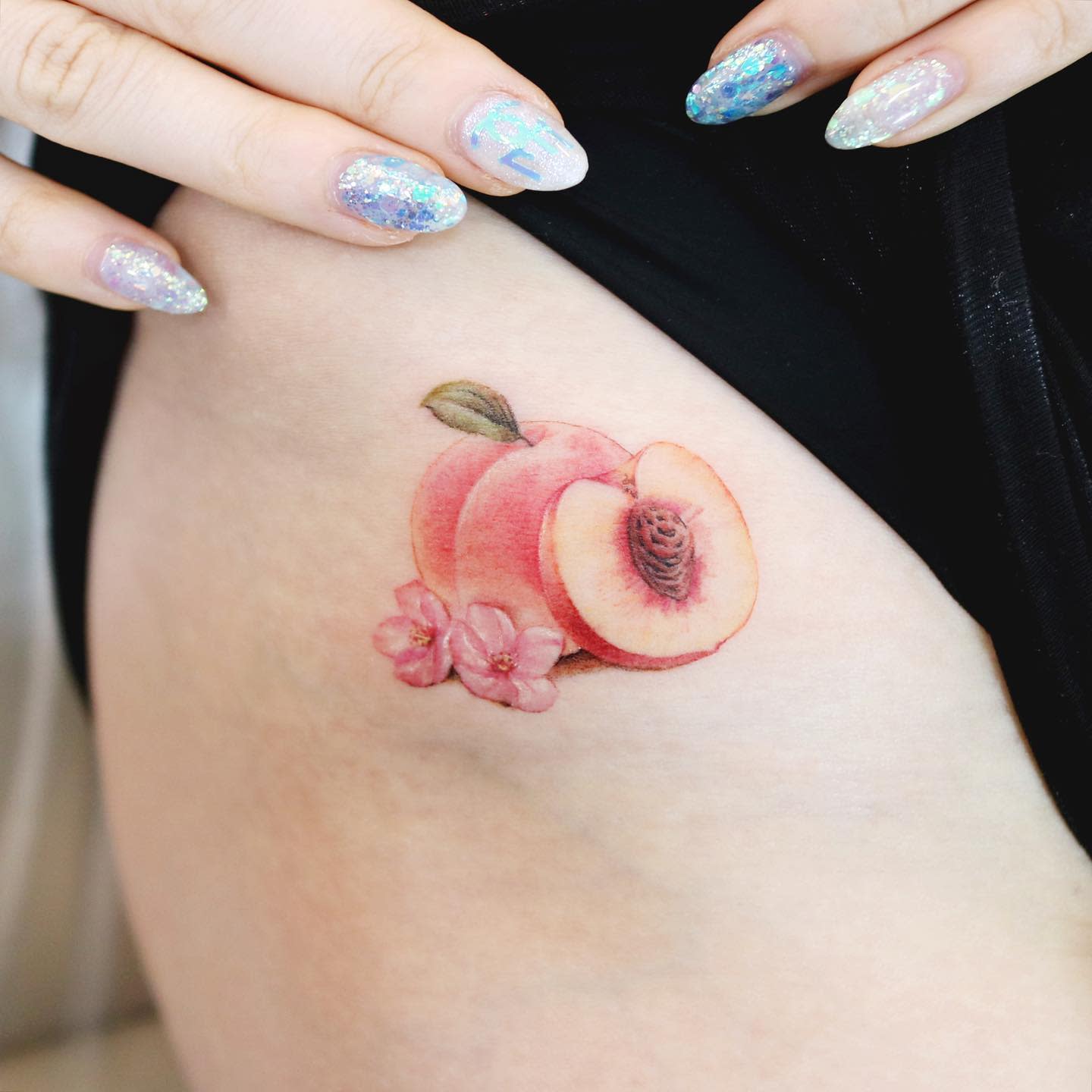 A tattoo of a peach with pink flowers on the inner thigh
